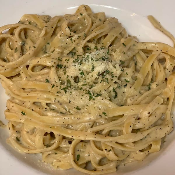 Creamy fettuccine alfredo pasta with parsley and grated cheese on a white plate.