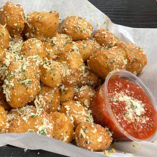 Golden-brown garlic knots, sprinkled with cheese and herbs, served with a side of marinara sauce.