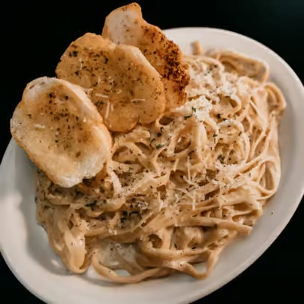 Creamy fettuccine alfredo with grated cheese and three pieces of garlic bread on a white plate.