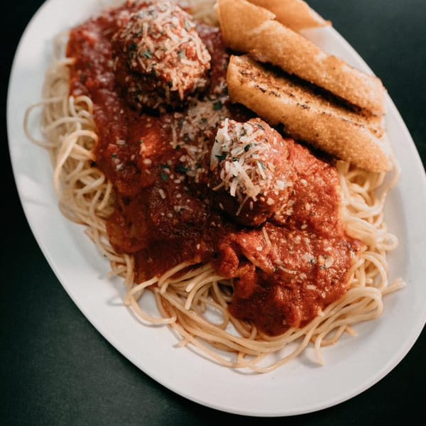 Spaghetti with meatballs, marinara sauce, grated cheese, and two garlic breadsticks on a white plate.